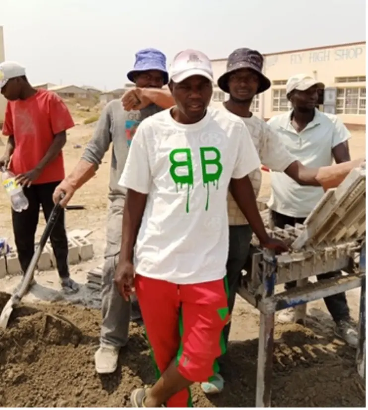 A team of young men at a brick-making press, one wearing a shirt with their team logo